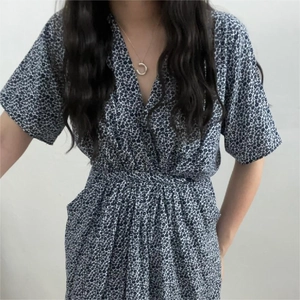 Detail of V-neck dark blue floral dress with short sleeves and a gold crescent necklace