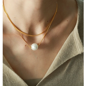Detail of double-layer gold chain necklace with white pearl pendant on model
