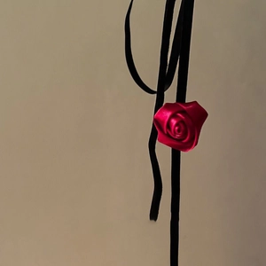 Detail of red fabric rose choker with long black ribbons on a neutral background