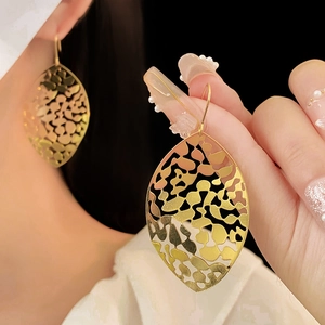 Detailed view of hollow gold leaf earrings with intricate cutout textures on ear hooks