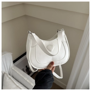 White minimalist saddle bag featuring a heart ornament and wide shoulder strap detail