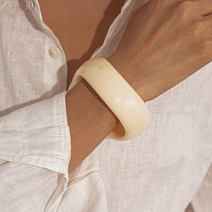 Close-up of wide cream acrylic resin bangle on model wearing a linen shirt