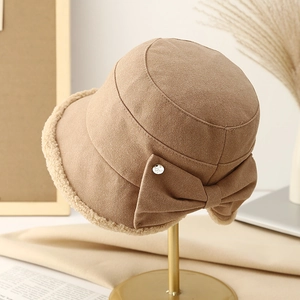 Beige winter bucket hat with faux fur trim and bow detail on a stylish gold display stand