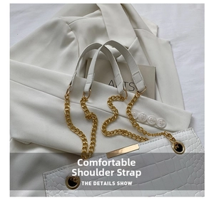 Detail view of white crocodile pattern texture and gold metal chain strap on handbag