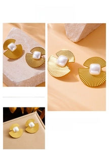 Close-up of golden fan-shaped earrings with square pearl inlay and striped metal texture