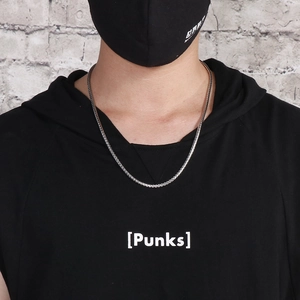 Silver stainless steel wheat chain necklace worn by a model against a grey wall