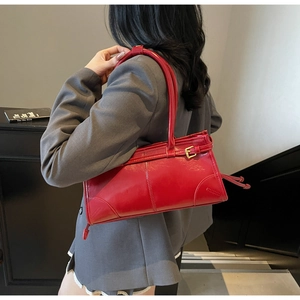 Model wearing a large red glossy leather tote bag against a modern grey suit