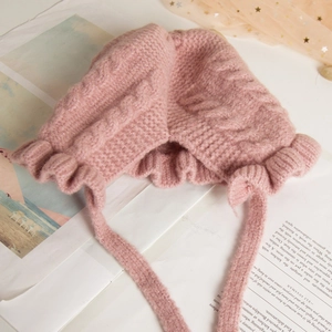 Close-up of pink knitted baby bonnet with delicate ruffled edges and soft chin straps