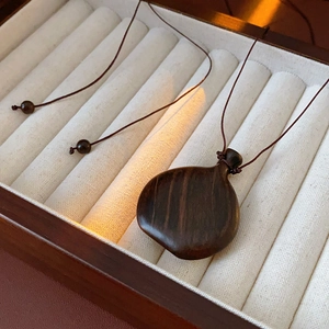 Macro view of pear-shaped dark brown wood pendant in a velvet-lined jewelry box
