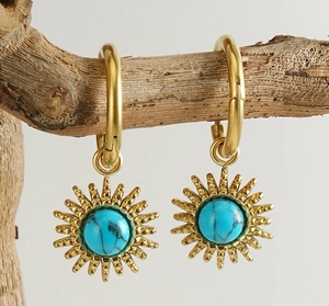 Detailed view of gold sunburst earrings with turquoise stone hanging on a branch
