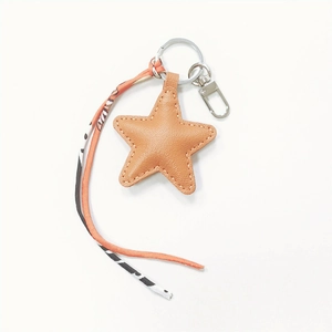 Detail of star-shaped orange leather keychain with patterned ribbon and metal clasp