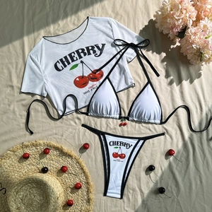 Flat lay of white three-piece cherry print bikini set with mesh cover-up and cherry charm