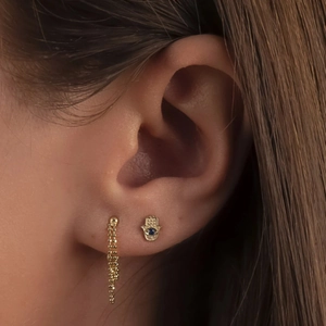 Detailed view of gold Hamsa hand stud with blue stone and chain earring on ear