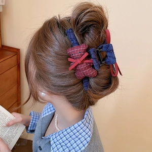 Detail of red plaid bear hair claw with ribbon bow on model's hair in a cozy setting