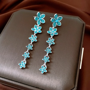 Macro detail of silver floral drop earrings with turquoise zircons on brown silk