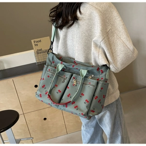 Detail of grey-green tote bag with cherry print showing multiple zipper pockets and wide strap
