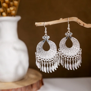 Detail of silver ethnic earrings with peacock leaf hollow pattern and tassel on wooden branch