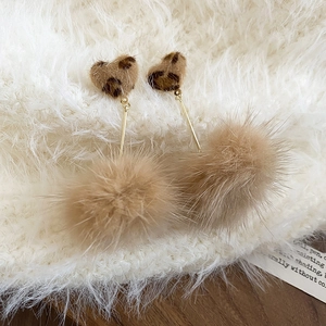 Detail of leopard print heart and khaki fur pom-pom earrings on soft textile background