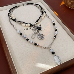 Close-up of layered bohemian necklace with butterfly coin, black gem, and leaf charms