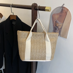 Detail of hand-woven straw tote bag with wide canvas straps hanging on a wooden hanger