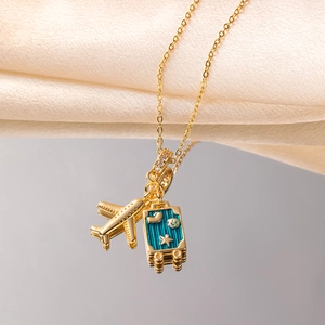 Gold airplane and blue suitcase travel pendant necklace on a mirrored surface