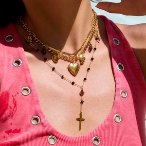 Detail of layered gold necklaces featuring heart, cross, and key charms on a model