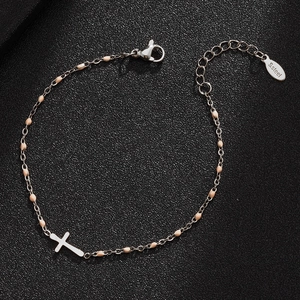 Detail of stainless steel cross charm bracelet with pale pink beads on dark surface