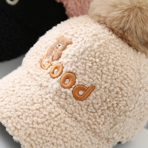 Detail of embroidered teddy bear and GOOD lettering on soft beige fleece baseball cap
