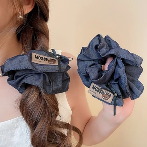 Detailed view of dark blue denim scrunchie with cute bear label and black ribbon accent