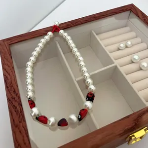 Detail of ladybug pearl necklace with red and black beads in a vintage wooden jewelry box