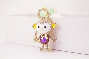 Detail of crystal monkey keychain in purple and gold leaning against a white gift box