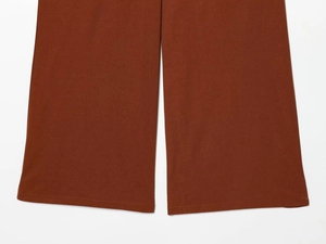Detail view of the stitching and wide-leg hem on dark brown fashion trousers