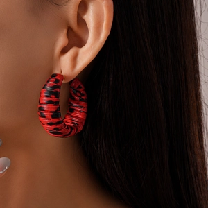 Close-up of a model wearing leopard print C-shaped earrings in red and black leather wrap