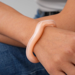 Close-up of peach pink wavy acrylic bracelet with marble texture worn by model