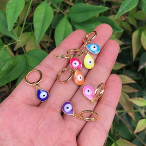 Golden hoop earrings with colorful enamel evil eye teardrop charms held in hand