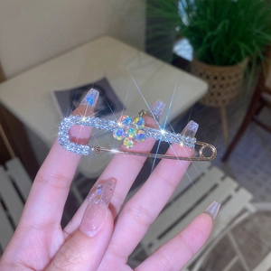 Detailed view of a gold safety pin brooch featuring a colorful gem flower and rhinestones