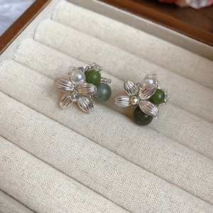Macro shot of flower earrings with white pearls and green agate on beige linen tray