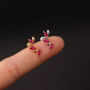 Macro shot of 16G stainless steel curved leaf ear studs with red zircon on fingertips