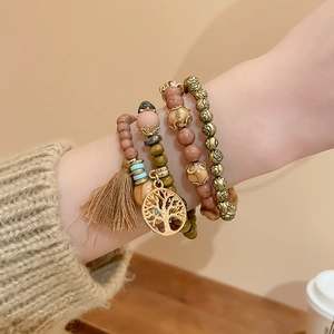 Detail of multi-layer sandalwood beaded bracelets with a gold tree of life charm and tassel