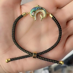 Detail eines verstellbaren Armbands mit Golddelphin und Muscheleinlage aus Seide