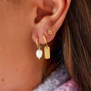 Close-up of golden earring set featuring a pearl pendant and a Dream engraved tag