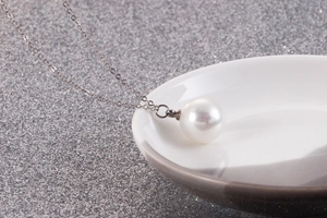Gros plan d'un pendentif perle blanche sur une chaîne en acier argenté et fond gris