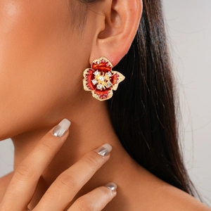 Close-up of gold flower stud earrings with red enamel petals and diamond accents