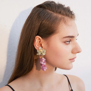 Detail of purple grape drop earrings with golden leaf design on a model