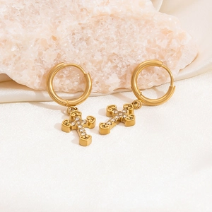 Gold hollow cross earrings with zircon crystals on white silk fabric background