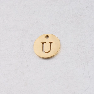 Vue macro d'un pendentif rond de 12mm en acier doré avec lettre U ajourée pour bijoux DIY