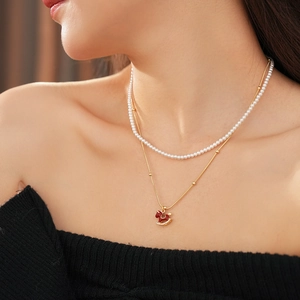 Close-up of double-layered necklace with white pearls and red rocking horse pendant
