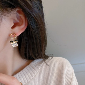 Gros plan de boucles d'oreilles nœud doré avec grand cristal carré porté