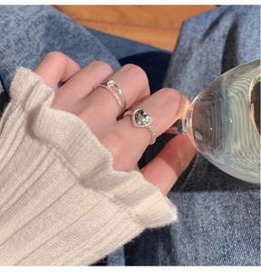 Close-up of a hand wearing a heart-shaped silver ring and a double-layered band