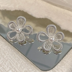 Detailed view of silver hollow flower stud earrings with a central pearl on white fur